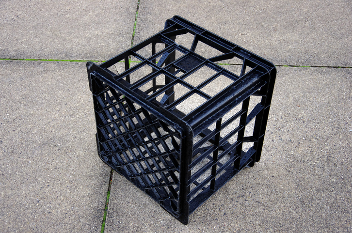 Black plastic milk crate on a concrete sidewalk