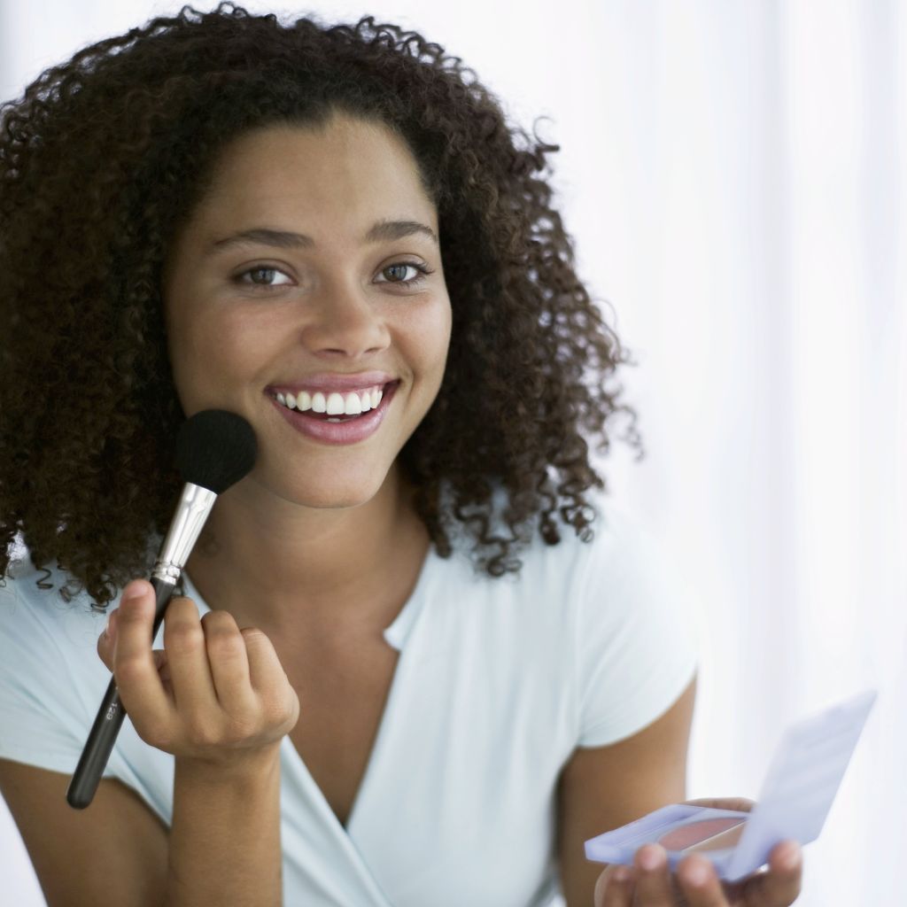 portrait of a young woman applying blush with a brush