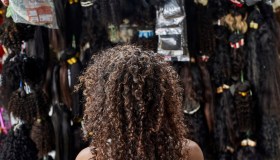 Young African woman from behind with curly hair in a wig shop.