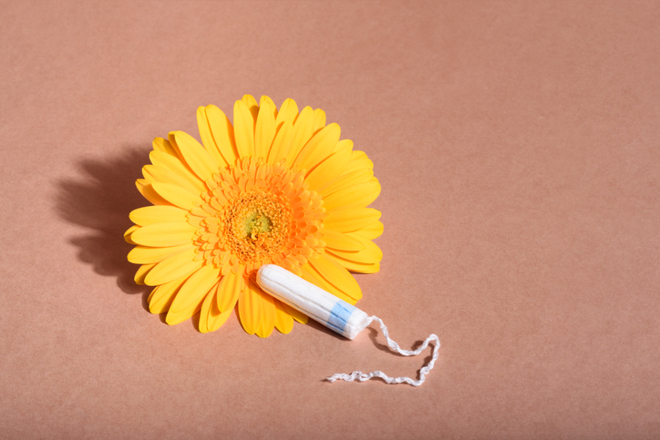 Medical female tampon with a yellow gerbera on a beige background. Hygienic white tampon for blood period. Cotton swab. Menstruation, girls, protection concept. Front view.