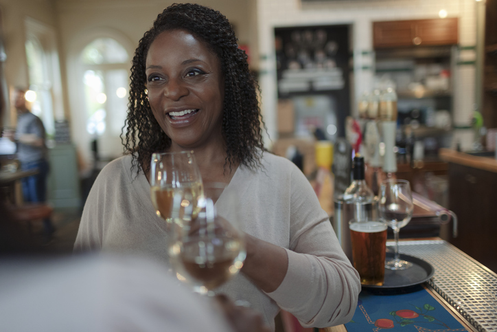 Smiling woman drinking white wine with friend at bar