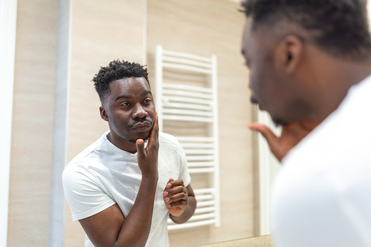Morning hygiene, Handsome man in the bathroom looking in mirror. Reflection of Africanman with beard looking at mirror and touching face in bathroom grooming