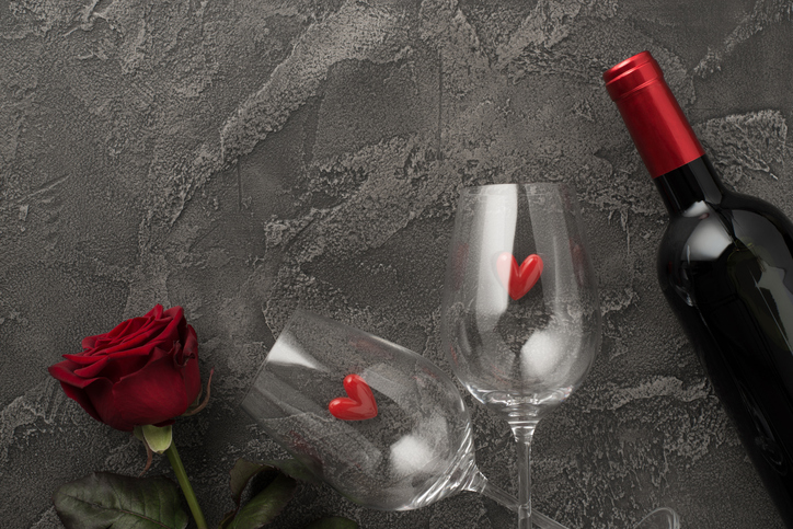 Top view photo of st valentine's day decorations two wineglasses with small hearts red rose and wine bottle on isolated textured dark grey concrete background with blank space