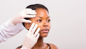 dermatologist checking young african american woman face skin