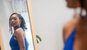 Create Your Own Style to Personality Development Make You More Attractive. A female African American in a tank top takes a look into a mirror and twists her body shape as she examines her reflection in a bedroom.