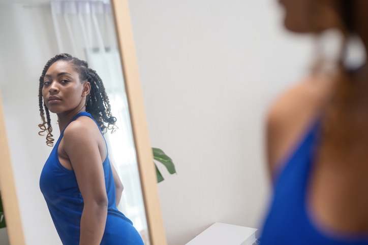 Create Your Own Style to Personality Development Make You More Attractive. A female African American in a tank top takes a look into a mirror and twists her body shape as she examines her reflection in a bedroom.