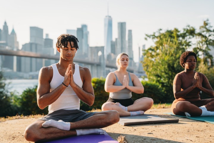 People are enjoying a yoga class outdoor in the city with New York City cityscape in the background