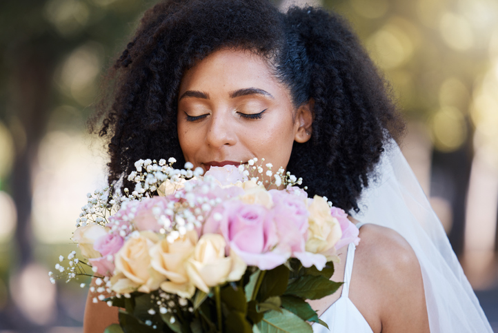 Eyes closed, bride and black woman with flowers at wedding outdoors. Face, marriage and beauty of female smelling floral bouquet of roses to celebrate at party, ceremony event or love celebration