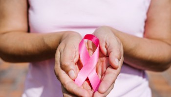 A woman holding a pink ribbon to signify Breast Cancer Awareness