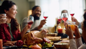 Roast turkey with family toasting during Thanksgiving meal Tat dining table.
