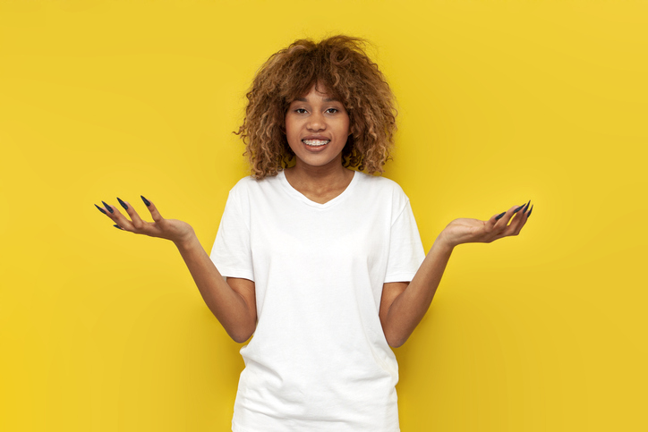 young curly american girl spreads her arms to the side and holds copy space on yellow isolated background