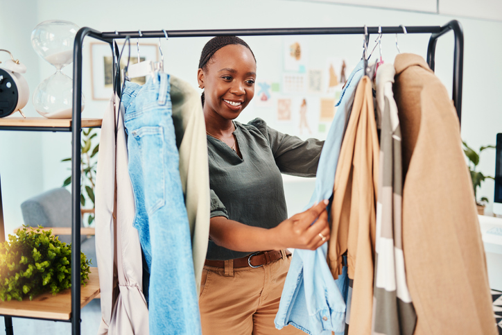 Customer, shopping and clothes rail with fashion, retail and choice for wardrobe, service and discount deal. Black woman client in shop for designer brand, happiness or product in luxury boutique