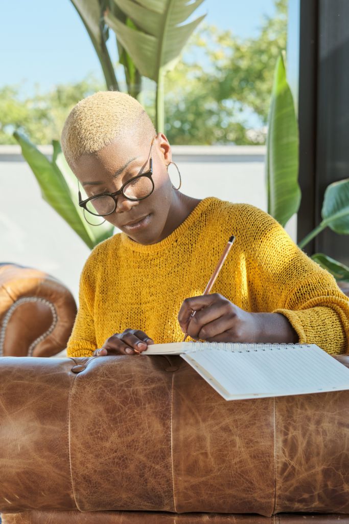 Focused woman writing in diary on couch at apartment