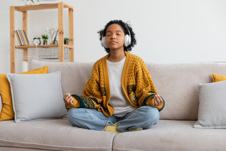 Yoga mindfulness meditation. Young healthy african girl practicing yoga at home. Woman sitting in lotus pose on couch meditating smiling relaxing indoor. Girl doing breathing practice. Yoga at home. shift from survival mode