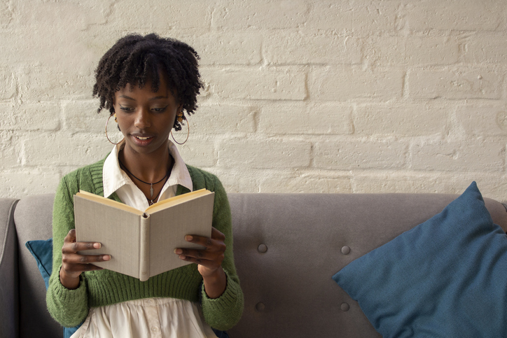 young african american woman sitting on a sofa reading a book attentively