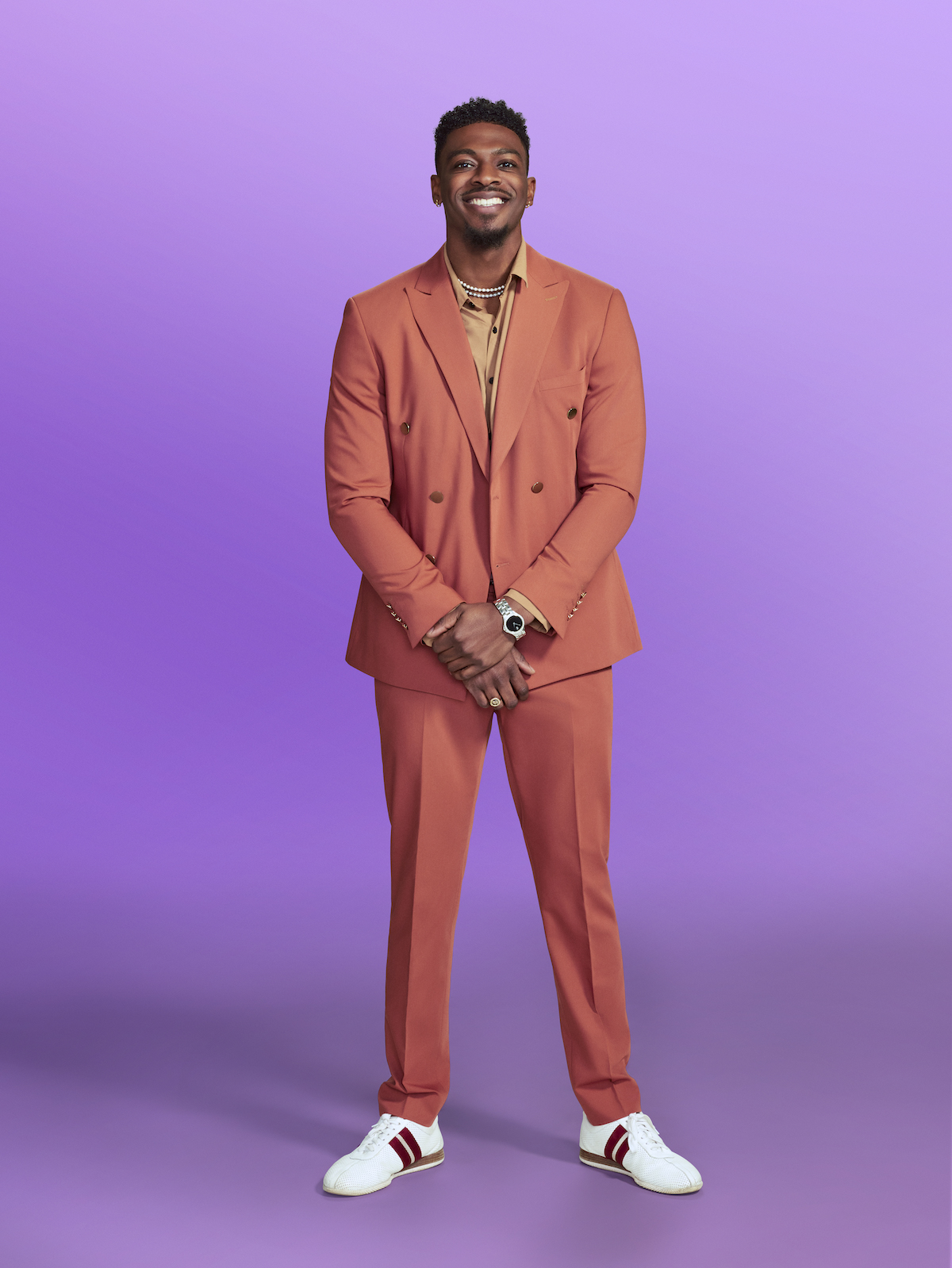 Clay Gravesande wearing a coral suit and sneakers in love is blind cast photos