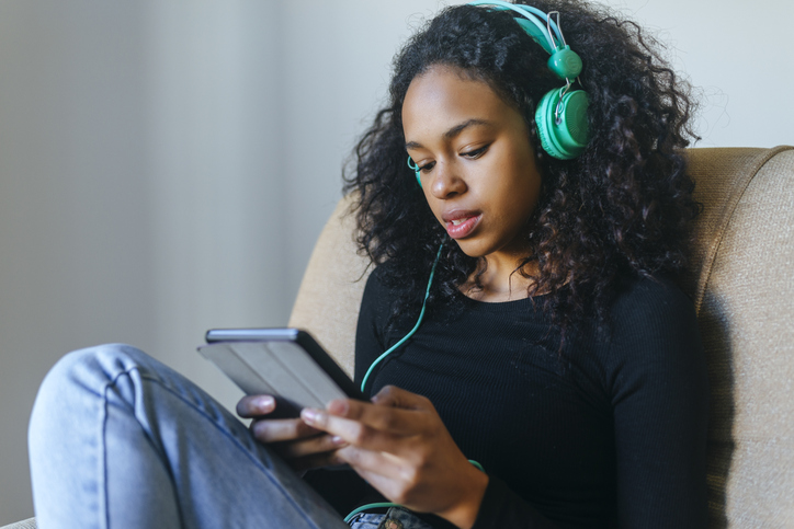 Portrait of young woman sitting in armchair listening music with headphones and tablet