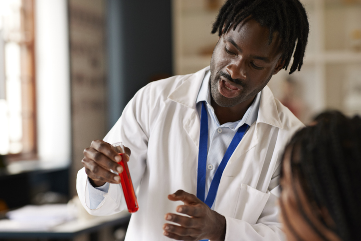 Male teacher explaining chemical in test tube to trans student