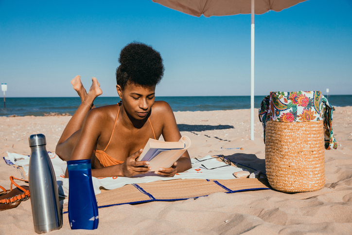 black Woman enjoying summertime at the beach reading a book