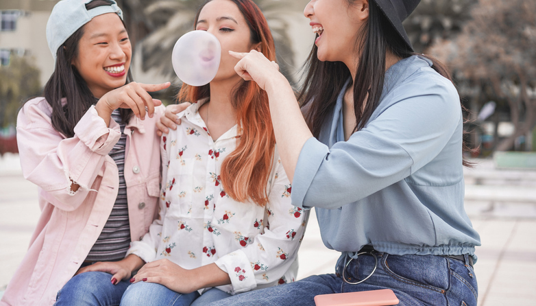 Trendy asian girls having fun together outdoor - Young women friends playing with bubble gum - Trends, youth, millennial generation and friendship concept - Focus on right person mouth