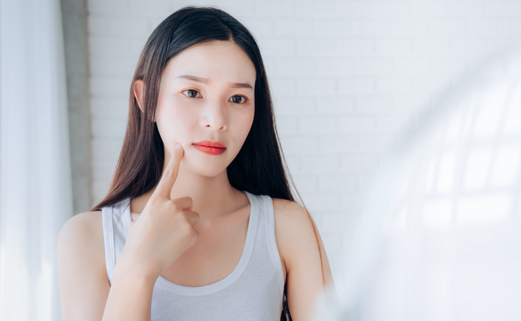 Young Woman Touching Face While Looking At Mirror At Home