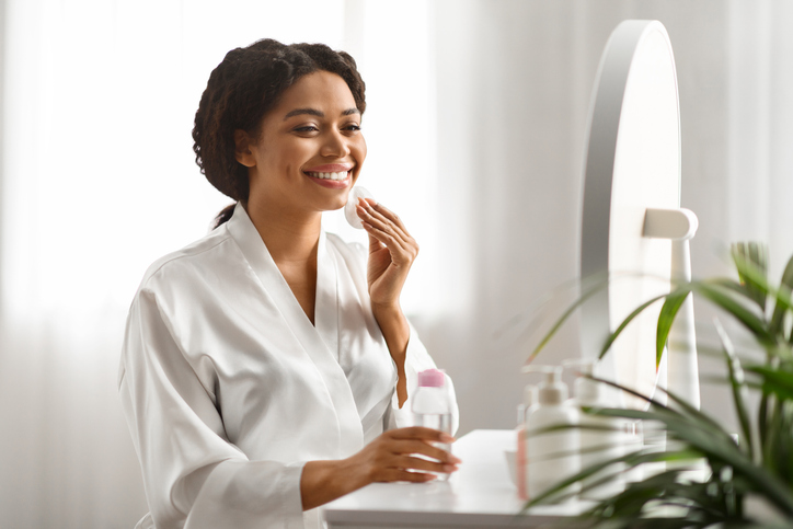 Black woman at home cleansing face with cotton pad and micellar water