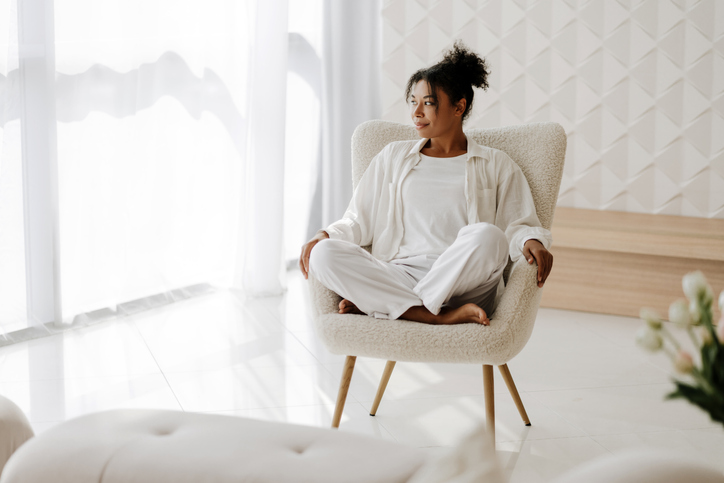 Young black woman relaxing at home sitting on armchair in white room