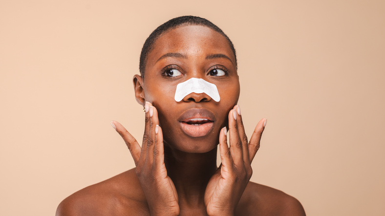 Black woman with short hair applies a nose strip, touching face.