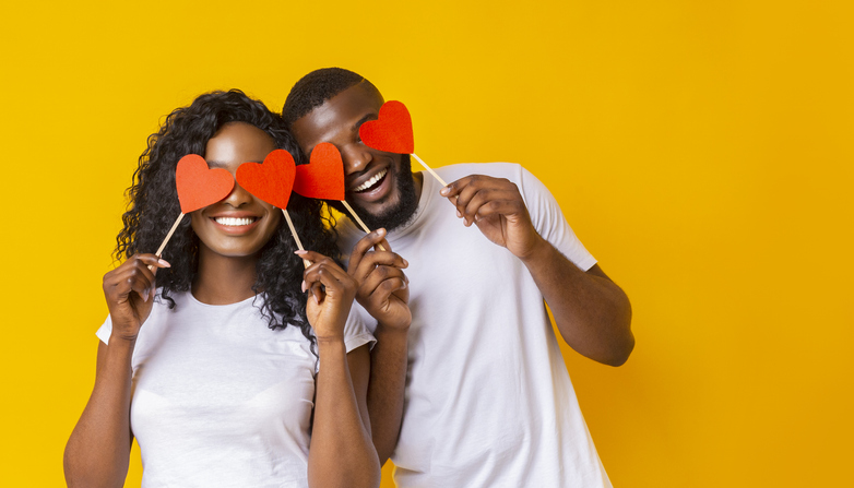 Young afro couple holding red love hearts over eyes