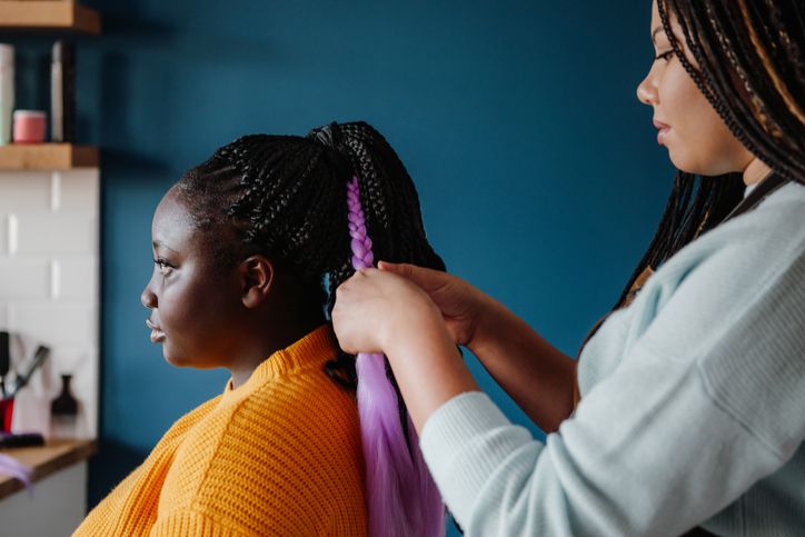 Close-up of hairdresser braiding hair to a young African woman in salon