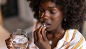 Woman Drinking Pill With Water at Office in a Relaxed Setting