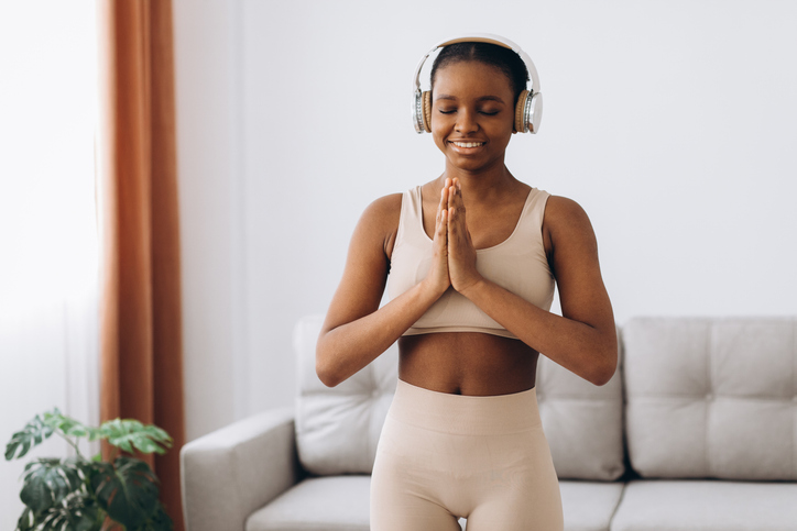 Young adult woman using headphones while meditating at home, finding inner peace and promoting self-care