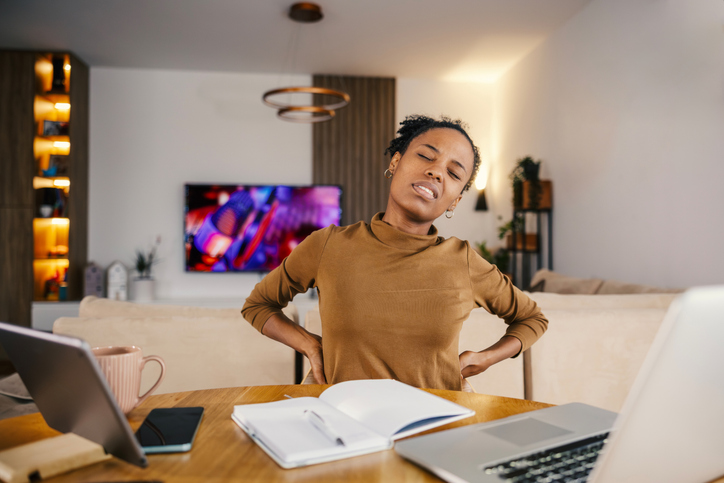 Young adult woman suffering from back pain working from home