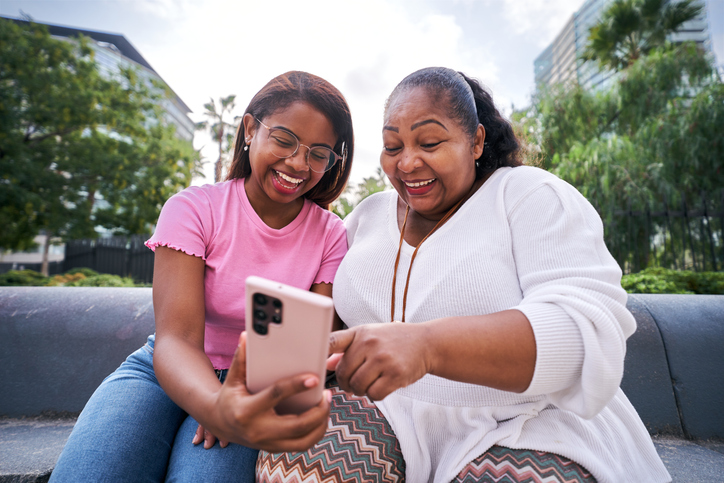 Two women smiling while looking at a smartphone outdoors