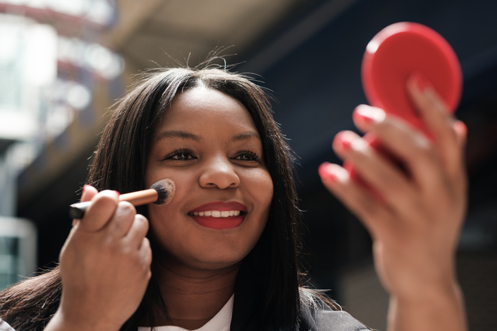 Businesswoman applying makeup with a brush and mirror, beauty products 