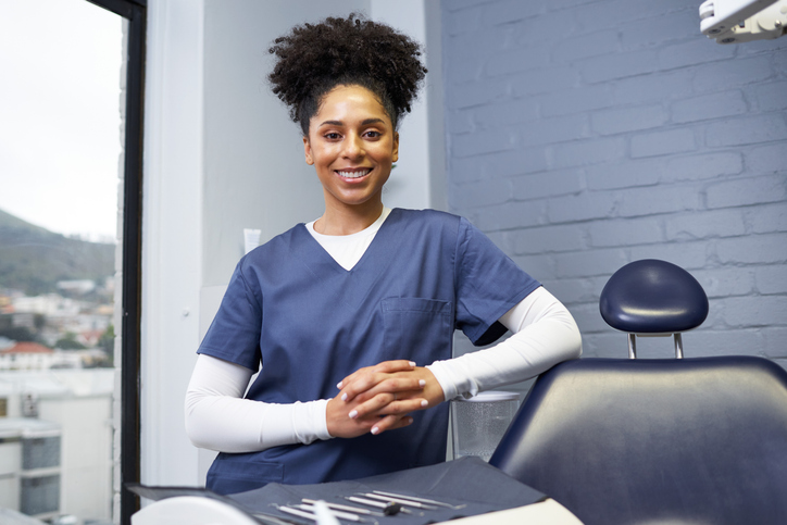 Smiling Dentist in a Blue Scrub Uniform Standing in a Modern Dental Clinic