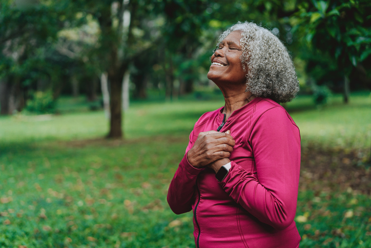 Elderly woman breathing fresh air in a public park with her hands on her chest