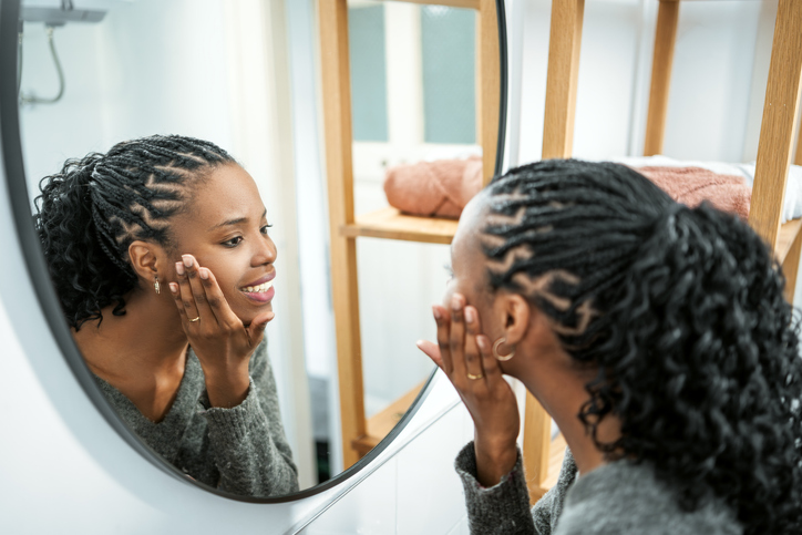 Young African woman applying hydrating cream to face
