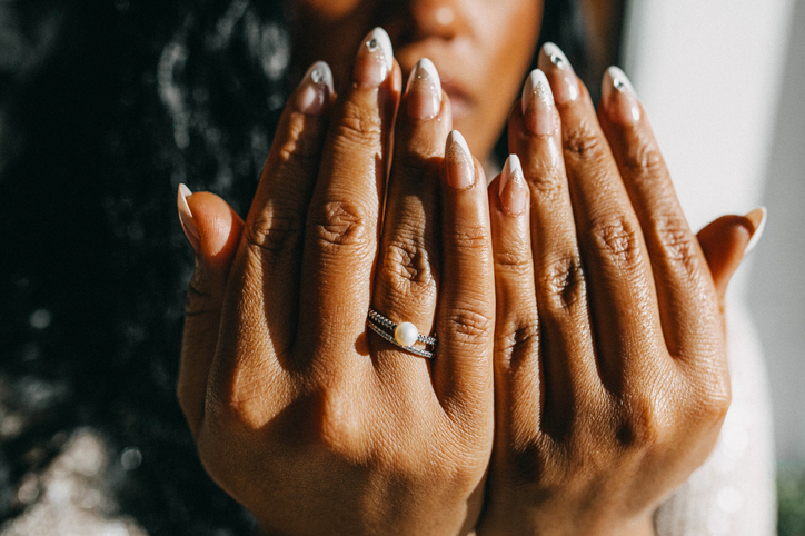 A close-up of hands with an elegant manicure, showcasing long, almond-shaped nails.