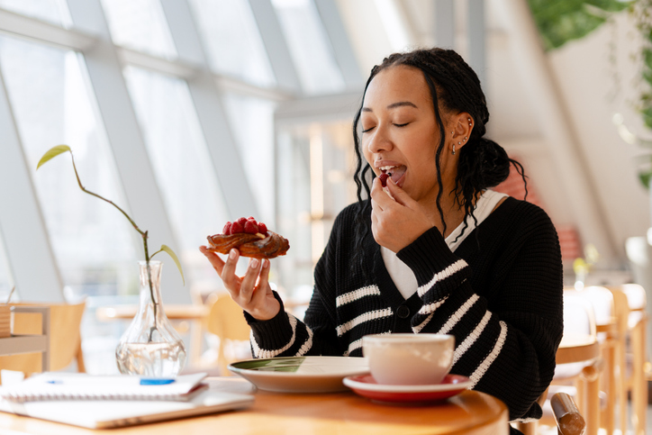Young happy African American woman enjoying raspberry pastry and coffee break