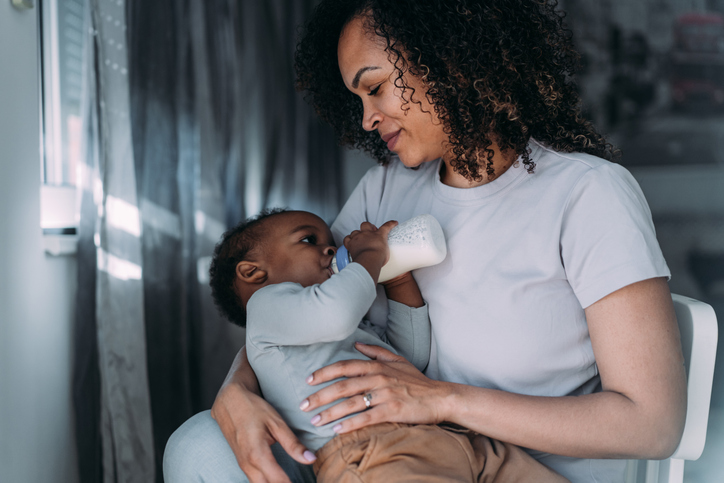 Mother feeds her baby boy with baby milk.
