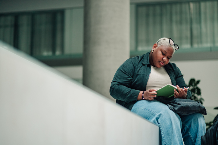 Young woman studying, reading book and concentrating in modern college library or university campus building