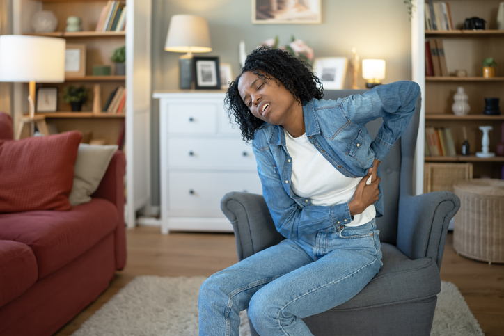 Young adult black woman suffering from back pain at home
