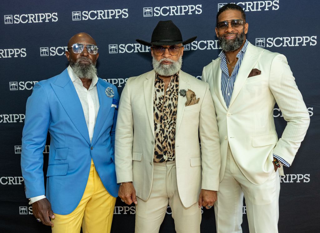 Three well-dressed men with beards and sunglasses posing in front of a Scripps backdrop.