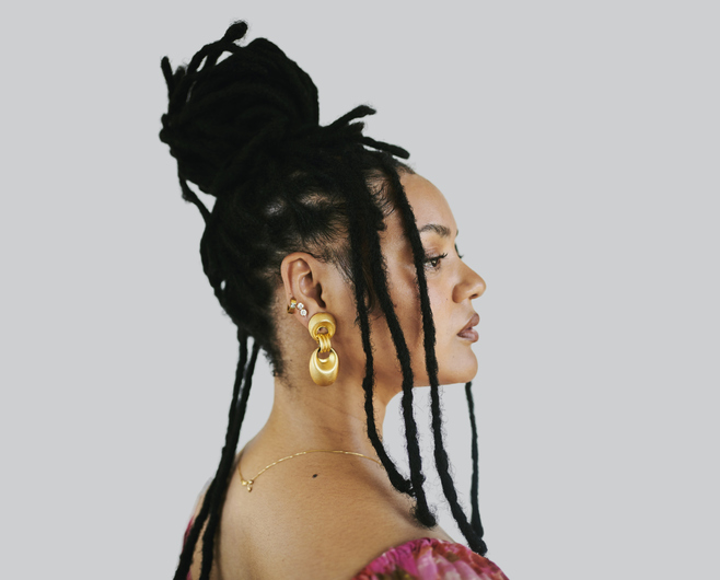 Serene African American Woman With Dreadlocks in Profile Wearing Gold Earrings and Pink Top