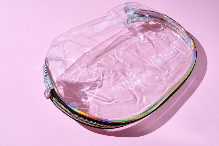 Empty plastic transparent bag for cosmetics on a trendy pink background with shadows and sunlight. Transparent makeup bag in flat style. Flat style