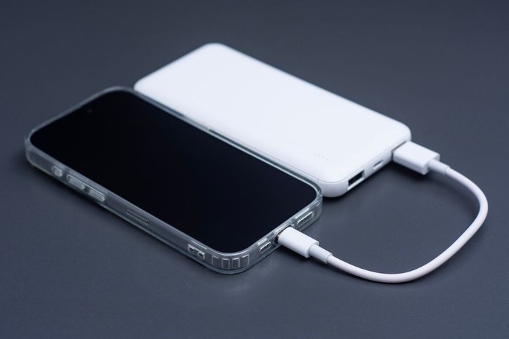Mobile phone connected to white external power bank with usb cable on dark background. Portable backup battery charging smartphone screen mockup for travel, technology or emergency energy.