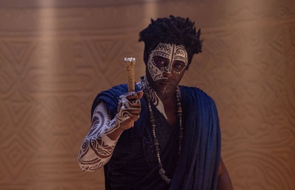 A person wearing face paint and holding a staff in a dimly lit setting.