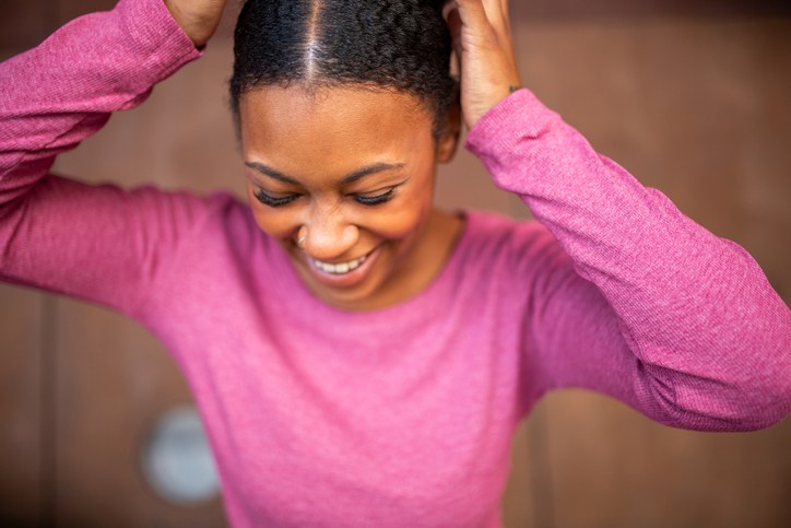 Smiling African American young woman in a pink sweater adjusting her hair