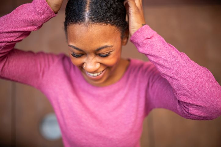 Smiling African American young woman in a pink sweater adjusting her hair